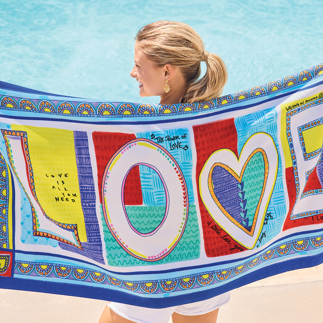 Woman holding a colorful Endless Summer Beach Towel with 'LOVE' design by a pool.