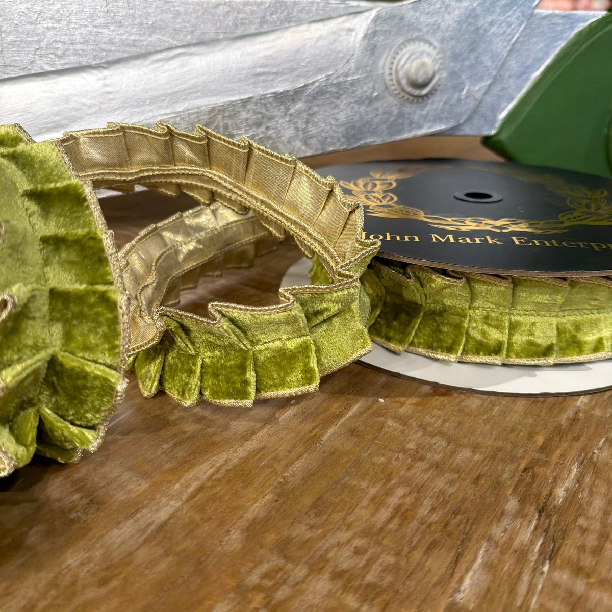 Apple green velvet pleated ribbon with metallic gold dupion backing on a spool and wooden surface.
