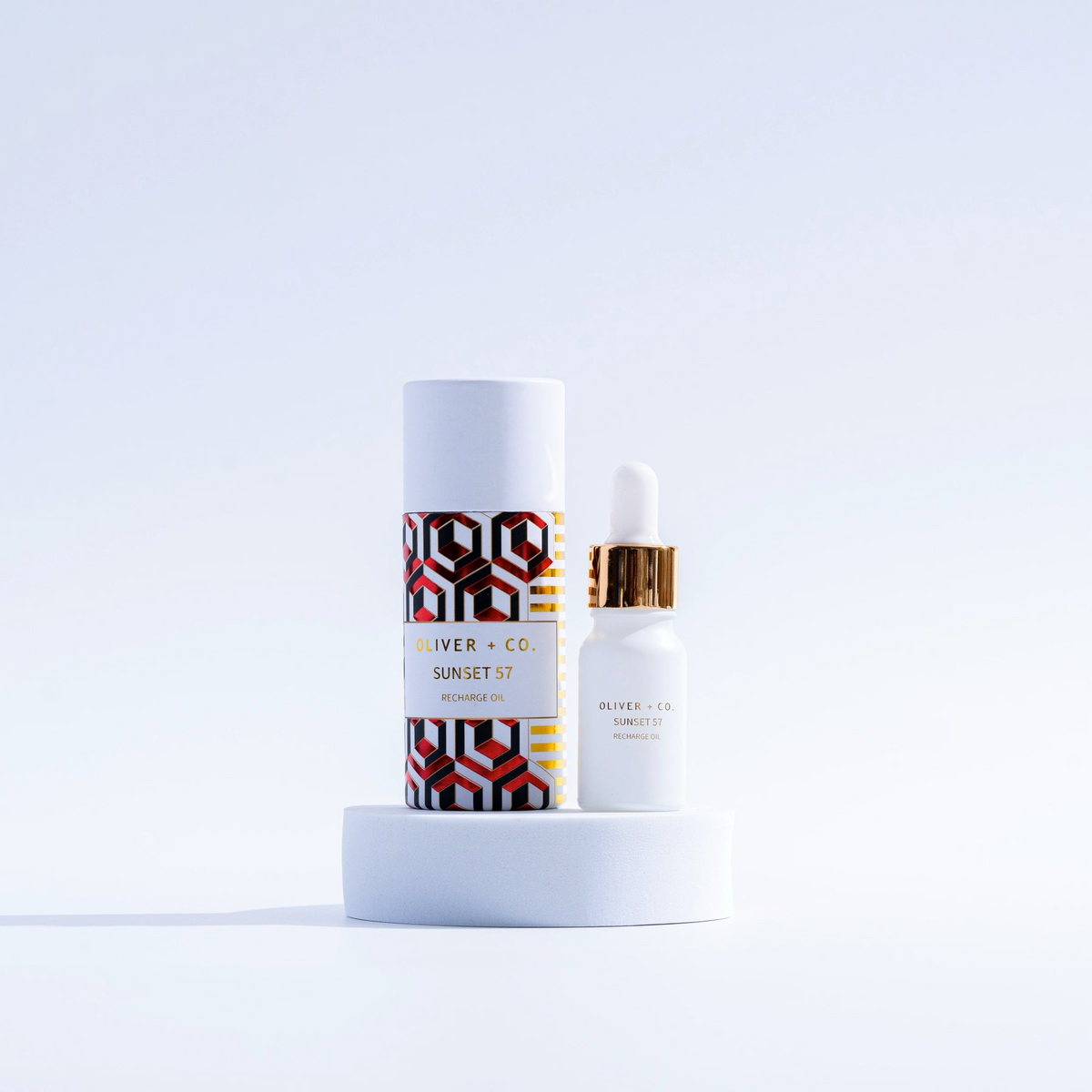 Oliver + Co. Sunset 57 Recharge Oil in a white dropper bottle next to its patterned cylinder box.