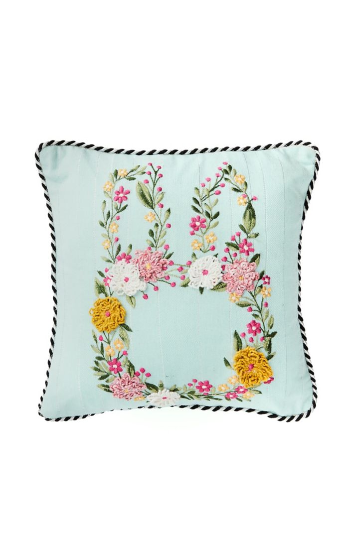 Light blue square throw pillow with a floral embroidered bunny silhouette and black corded trim.