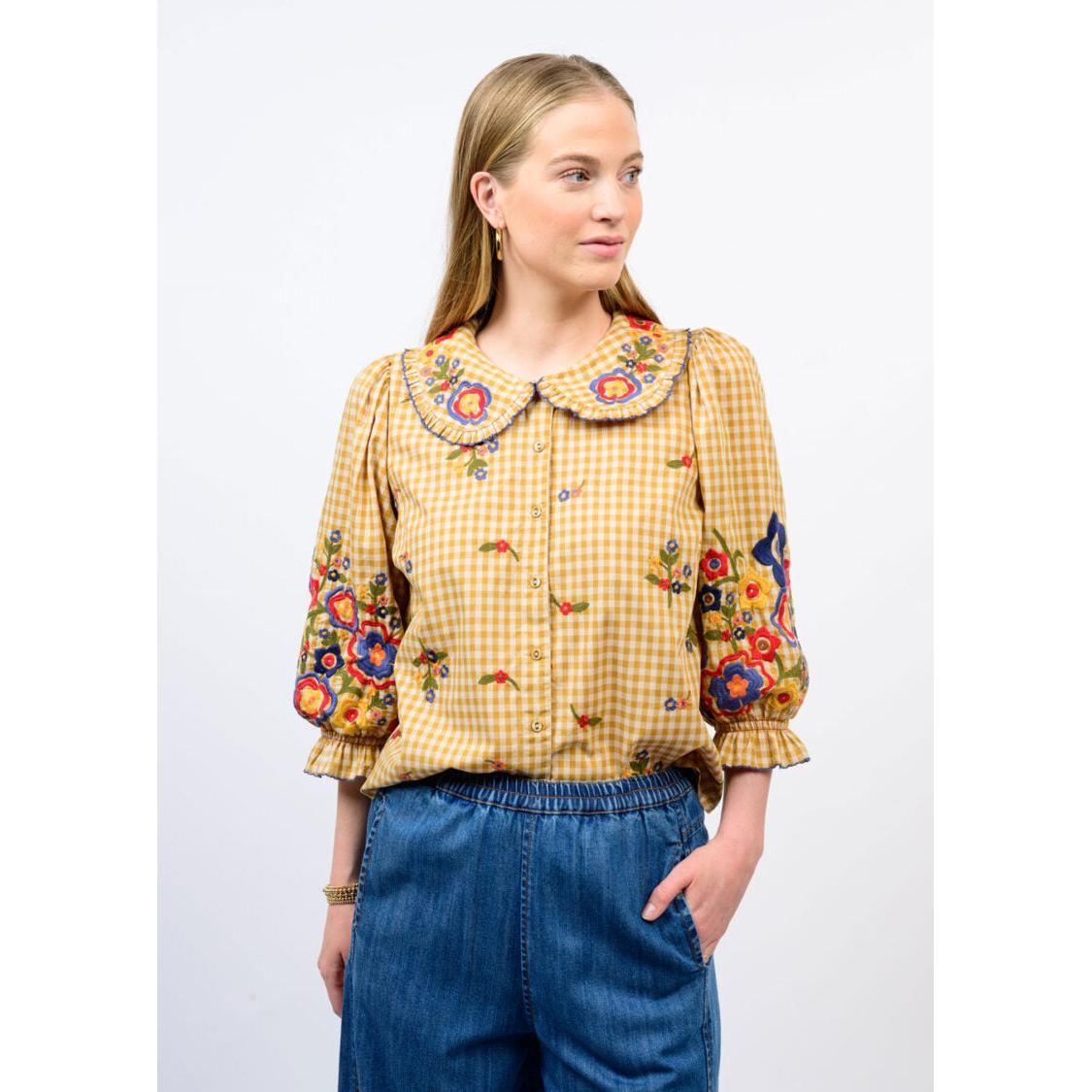 Woman wearing the Marian Check Garden Top, a yellow gingham blouse with floral embroidery.