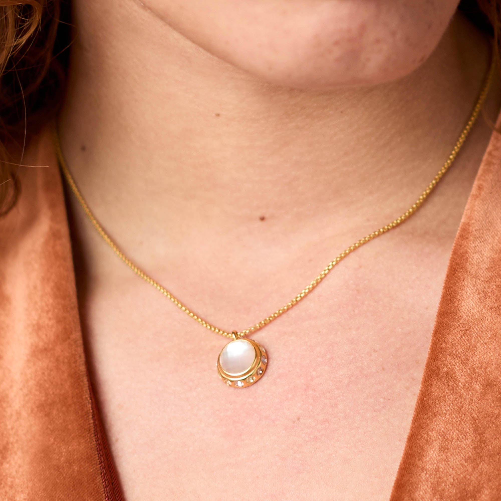 Rainbow Delicate Necklace with a gold chain and round white glass pendant on a person's neck.