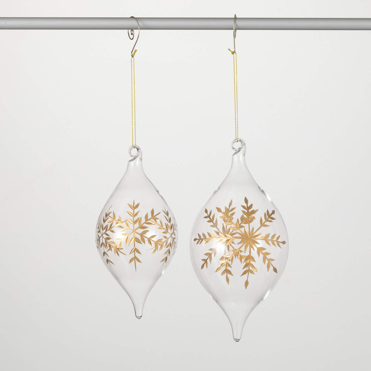 Two clear glass onion-shaped ornaments with gold snowflake patterns hanging from gold strings.