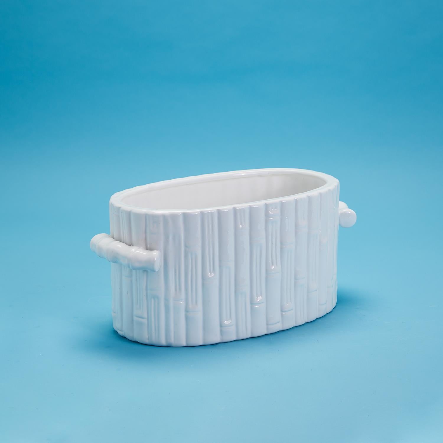 White ceramic faux bamboo oval centerpiece cachepot with handles against a blue background.