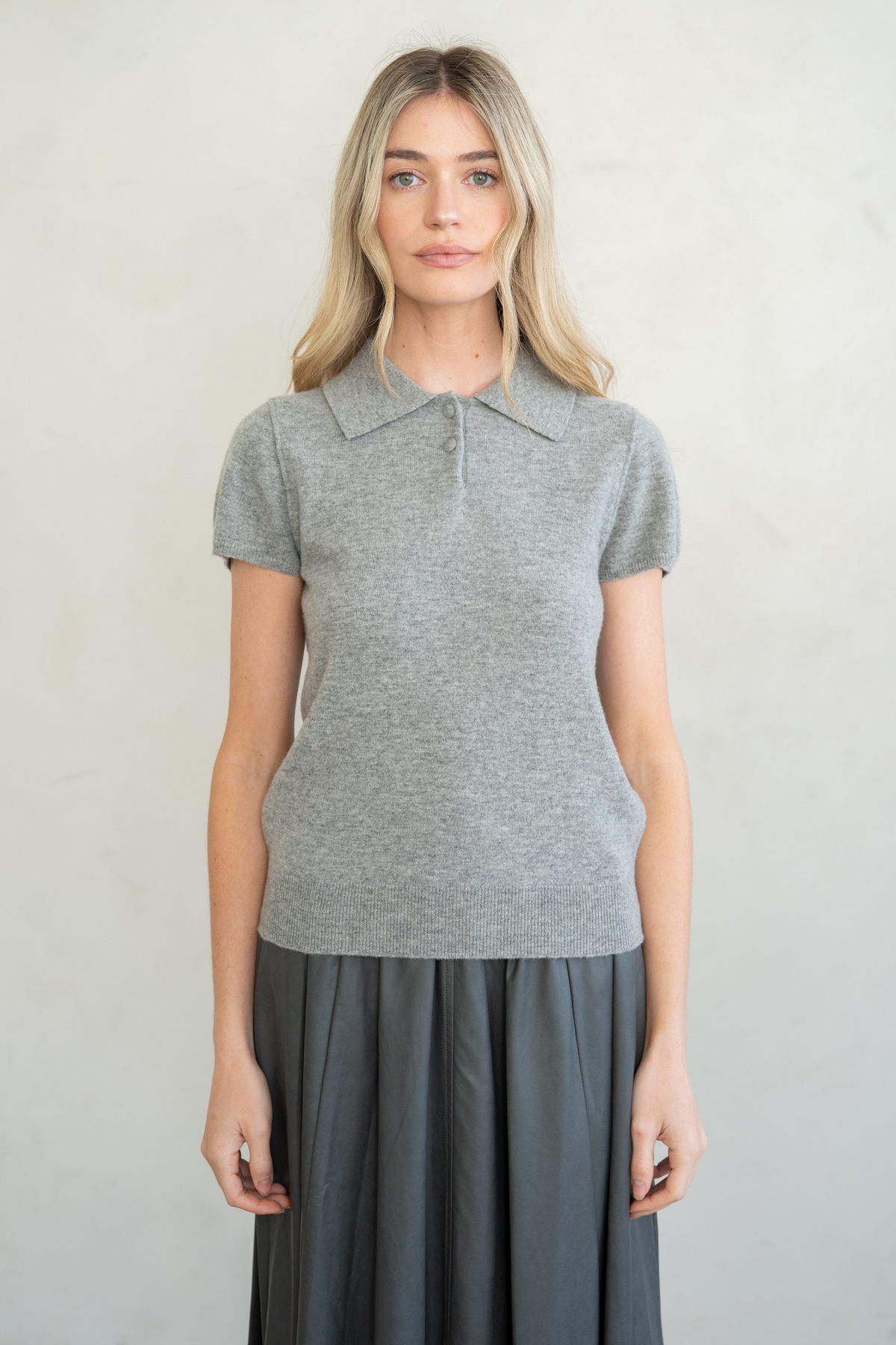 Woman wearing a grey Elise Refined Cap Sleeve Polo Sweater Top with a pleated skirt.