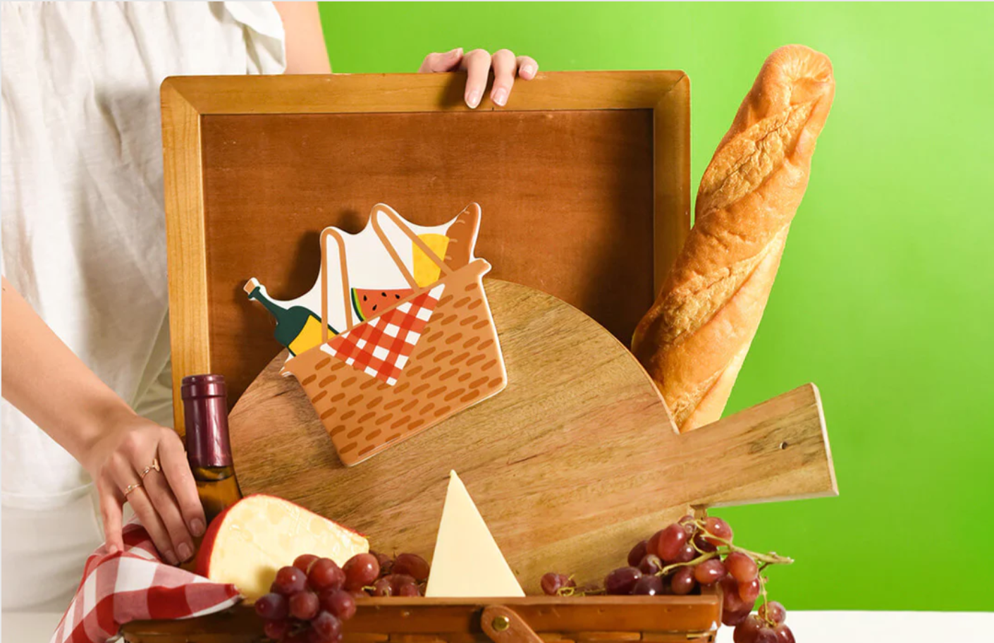 Ceramic picnic basket attachment with a checkered napkin, wine, and fruit on a wooden board.