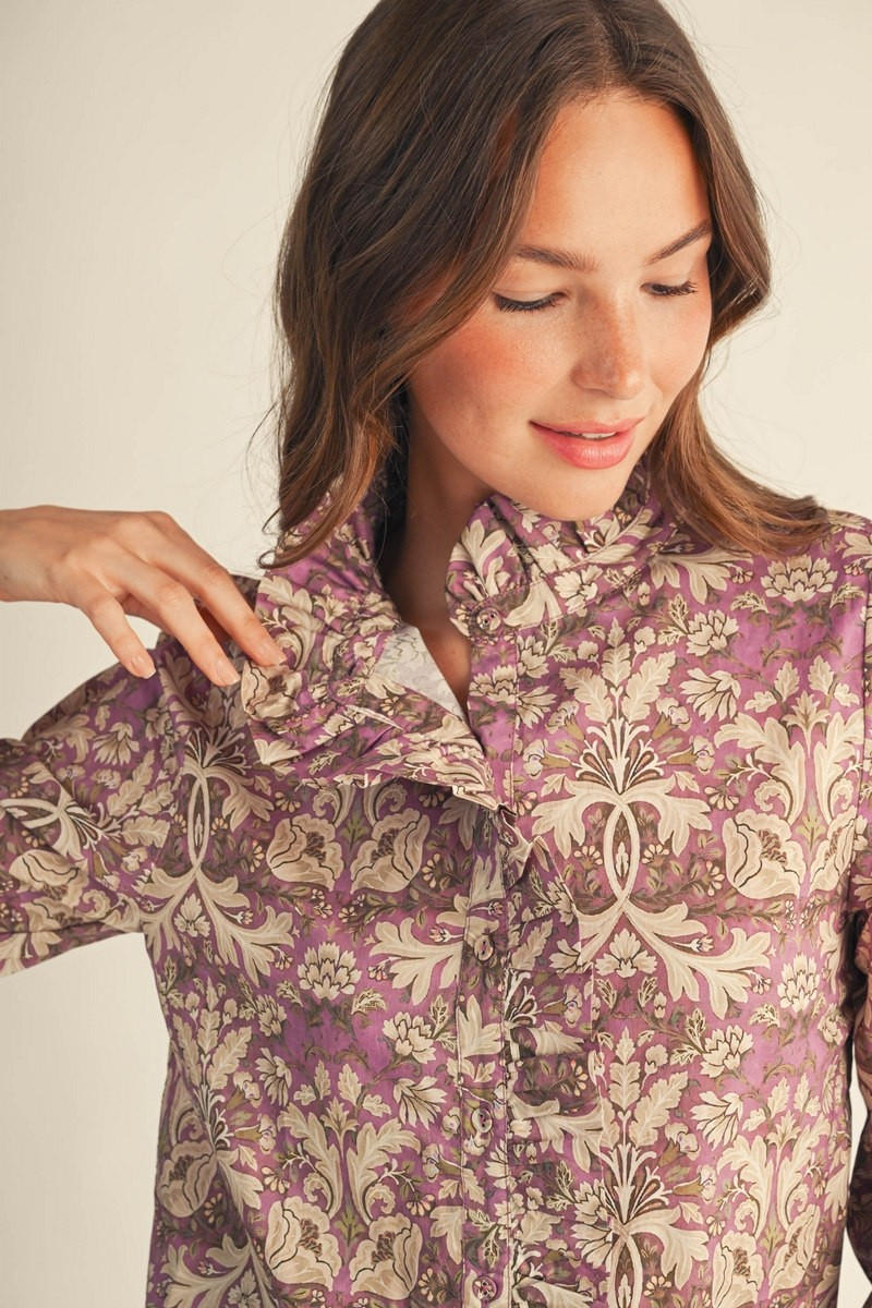 Close-up of a woman wearing a purple baroque floral blouse with ruffle collar and button-down front.