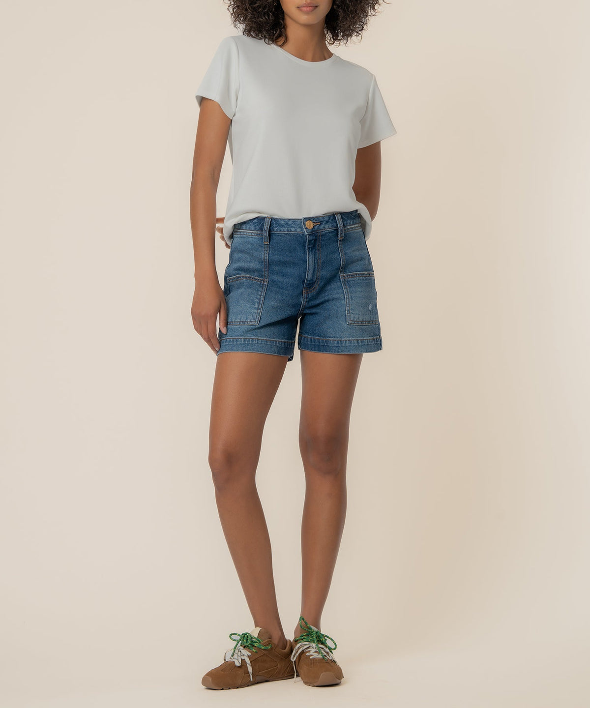 Woman wearing Jane high rise denim shorts with large pork chop pockets and a white t-shirt.