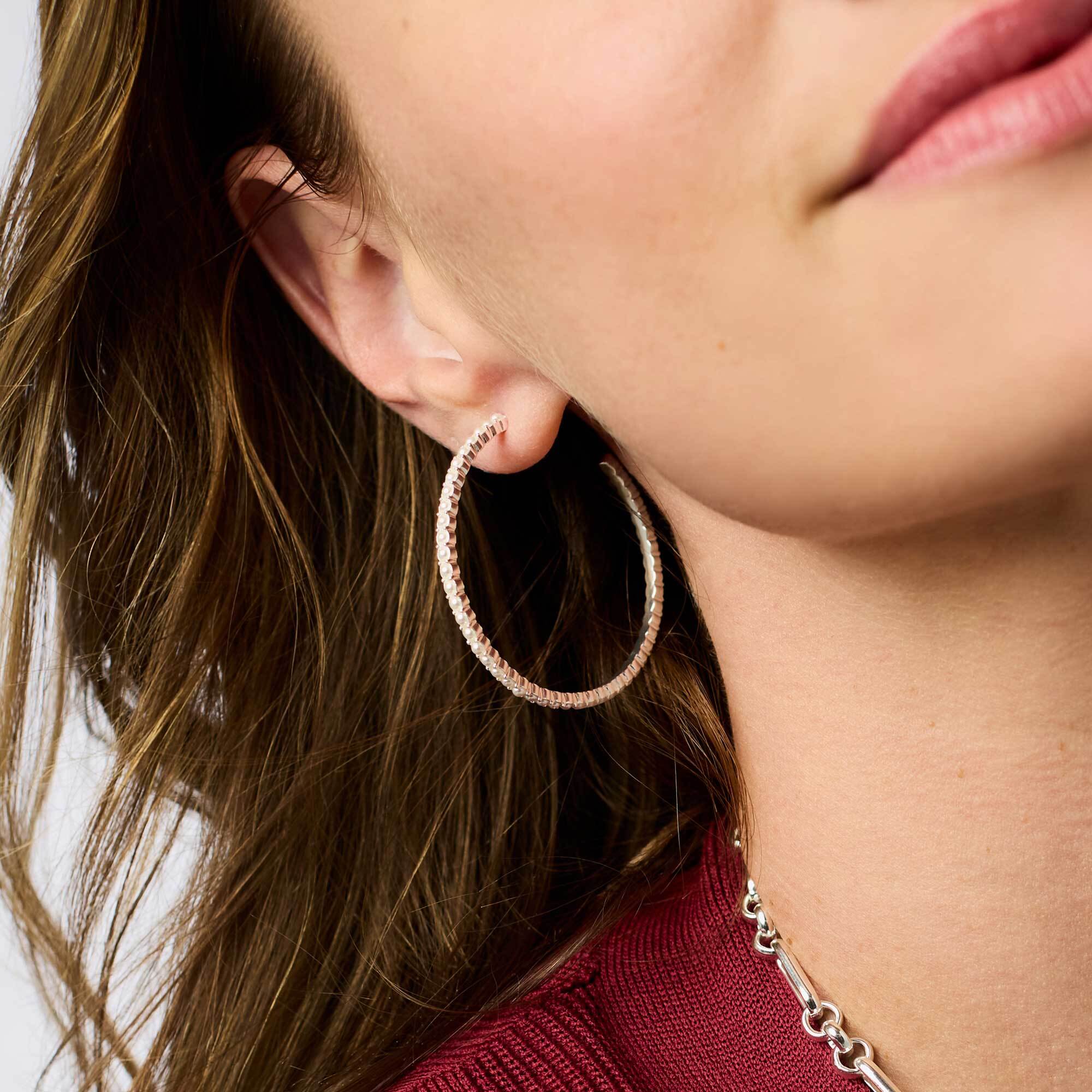 A person wearing a Juliet Hoop Silver earring featuring glass pearls and a silver-plated finish.