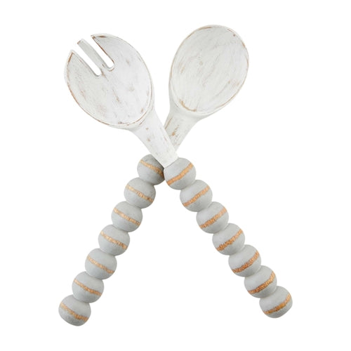 Wooden salad servers with white-washed tops and gray beaded handles with gold accents.