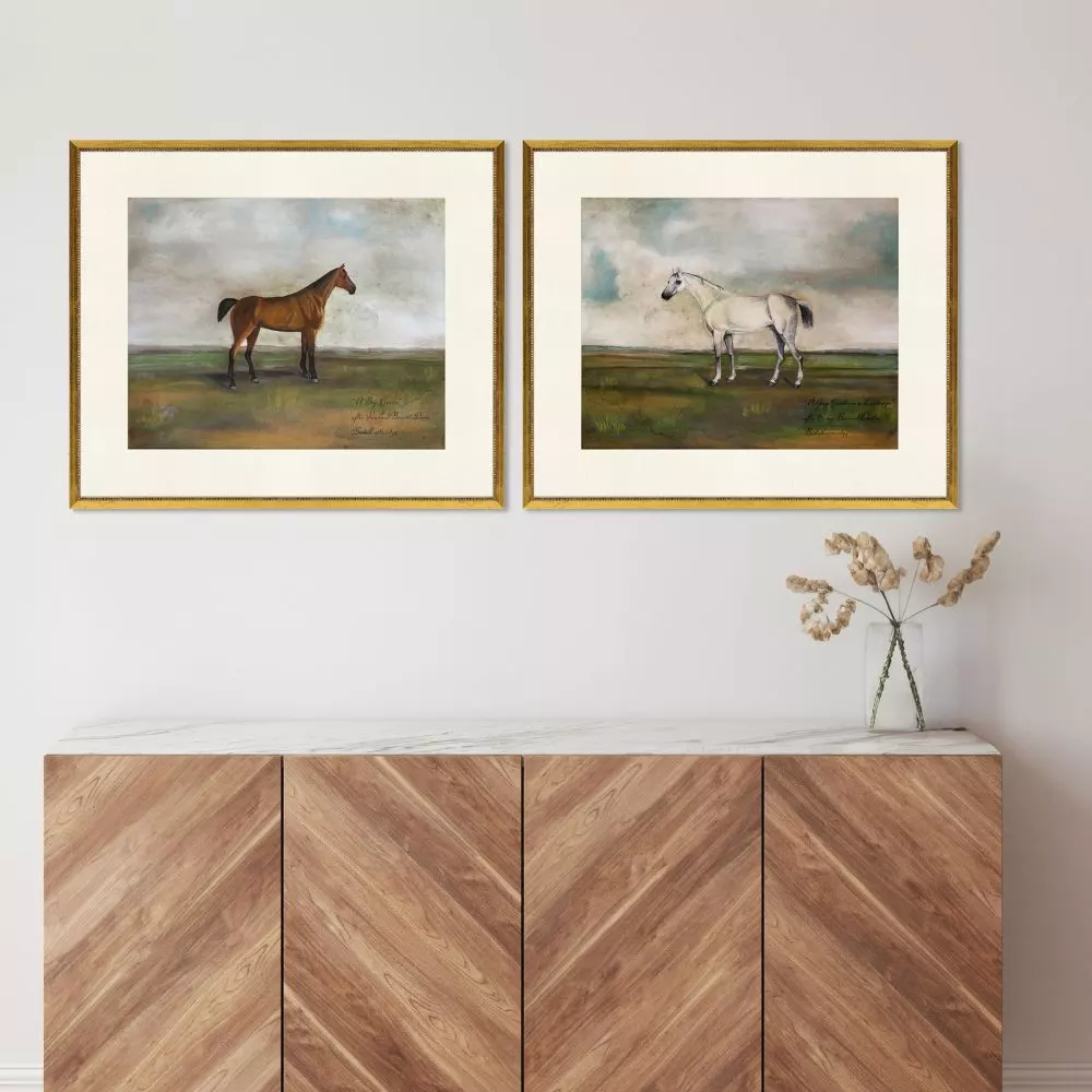 Two framed equestrian paintings of a brown and white horse above a wooden sideboard.