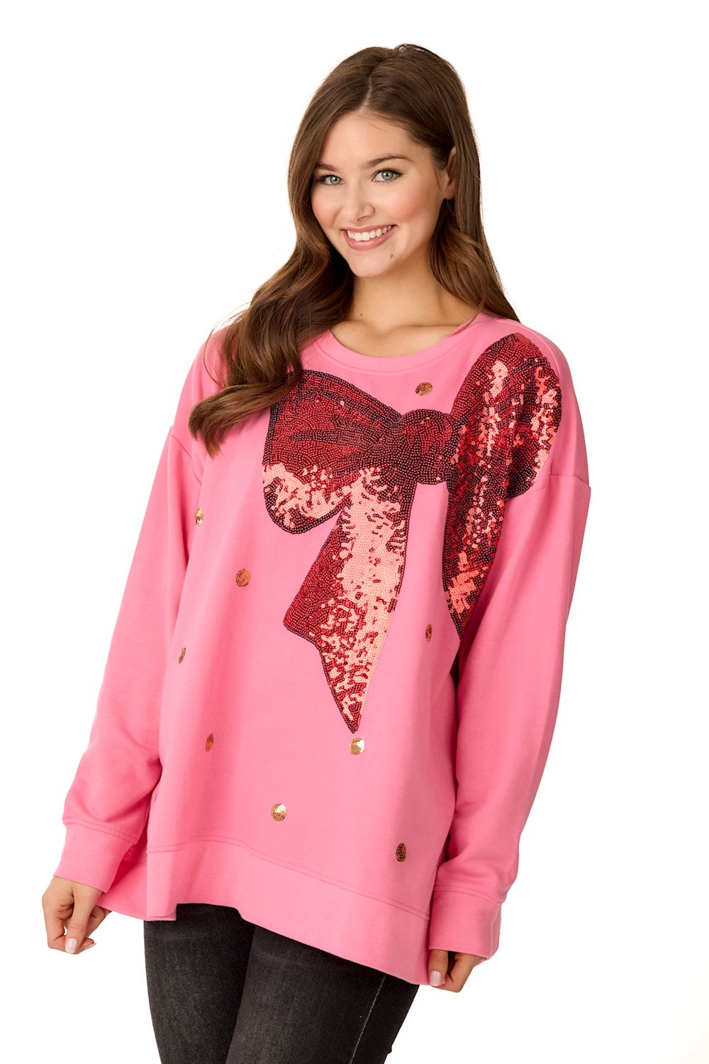 Woman wearing a pink oversized sweatshirt with a large red sequin bow and gold polka dots.