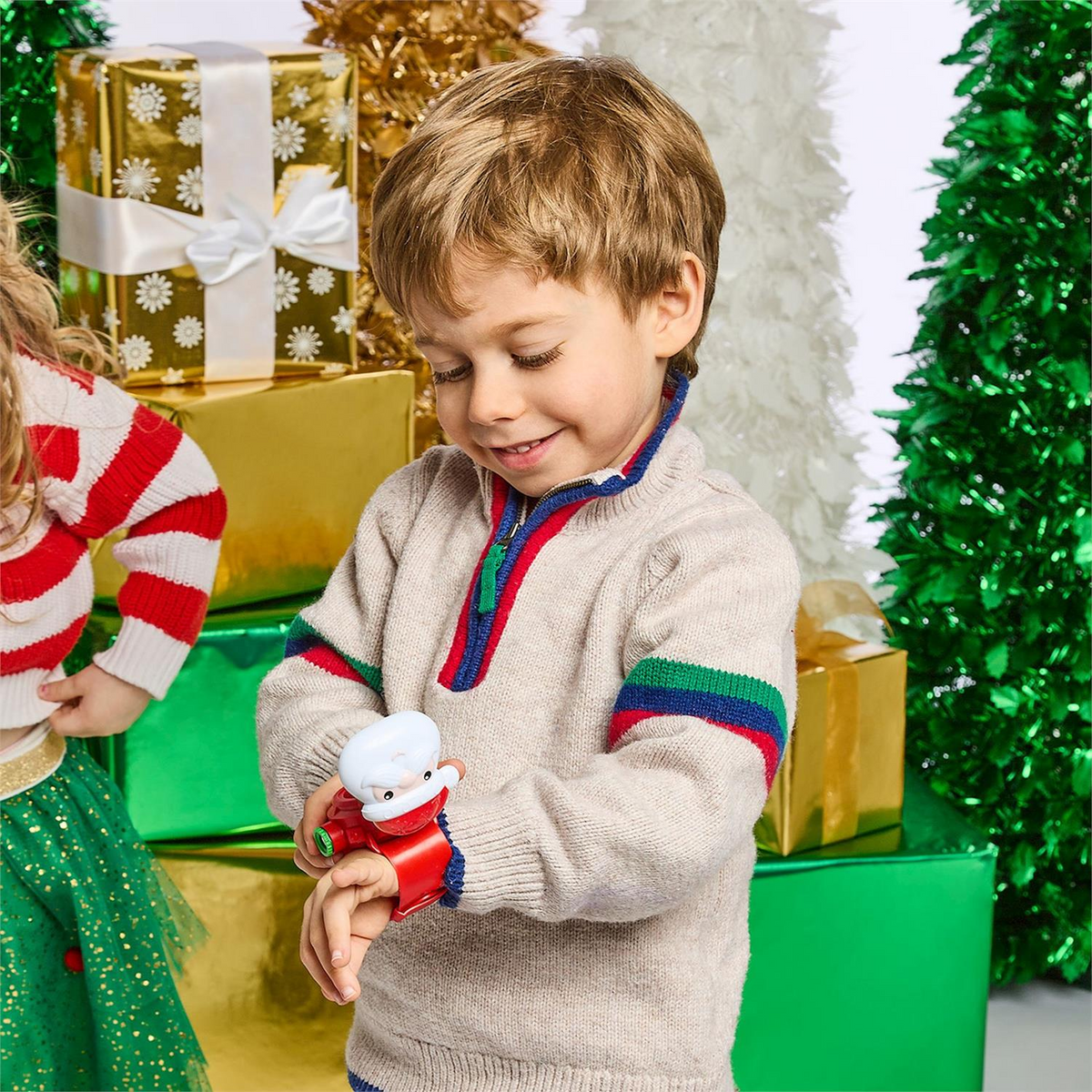 A young boy wearing a Santa digital watch with projector, standing in front of Christmas gifts.