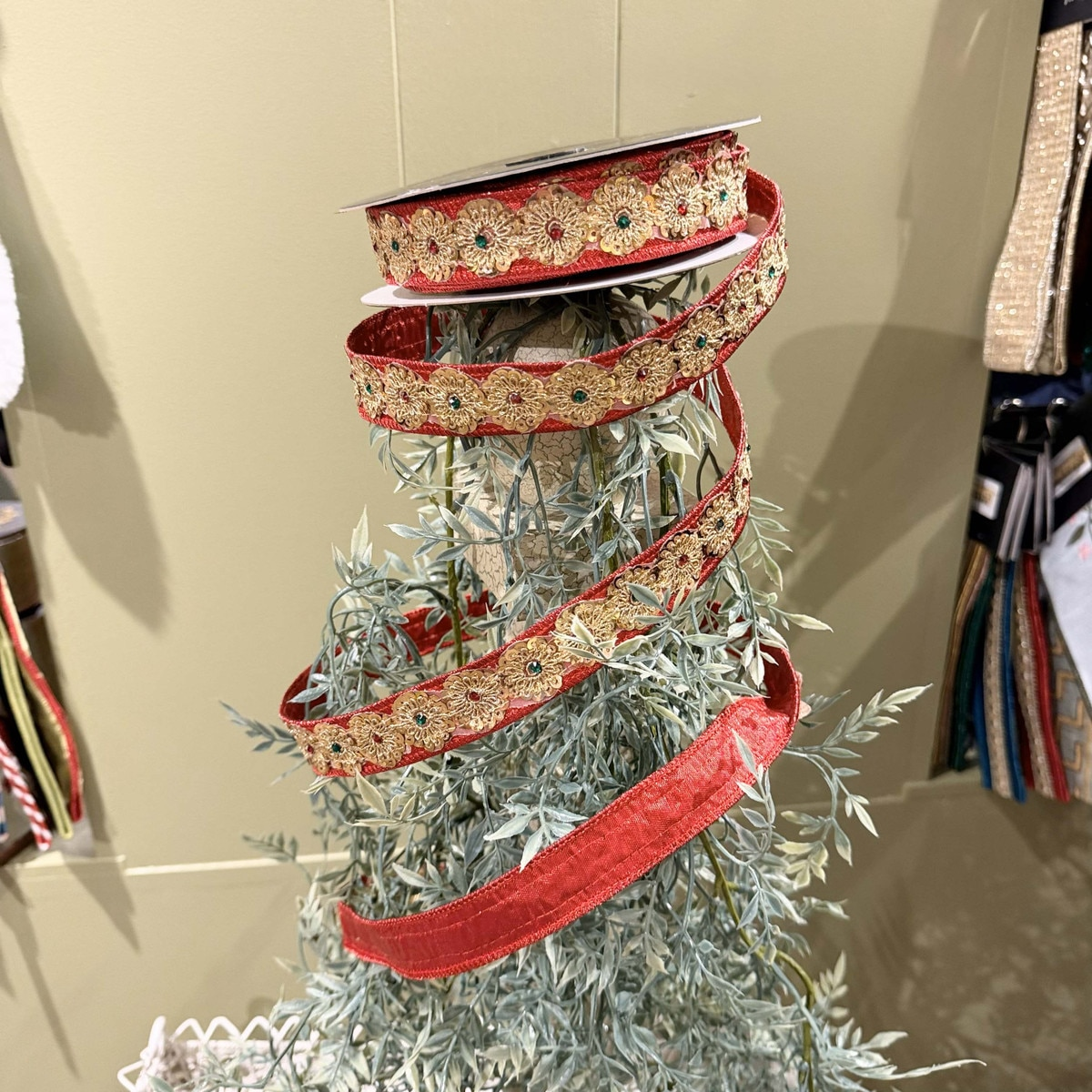 Red metallic dupion ribbon with gold sequin and jewel flower trim overlay on a spool.