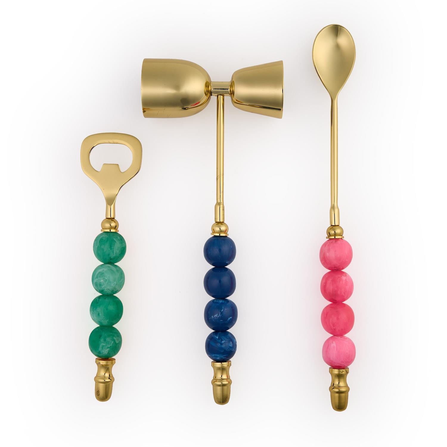 Gold bar set with a green bottle opener, blue jigger, and pink mixing spoon with beaded handles.