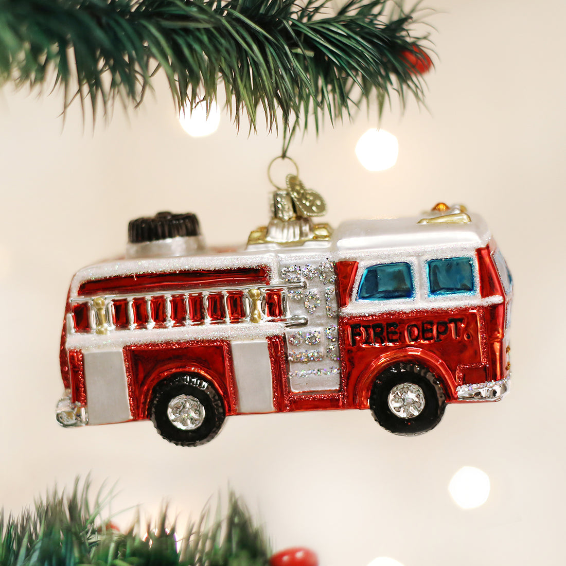 Red and white glass fire truck Christmas ornament hanging from a pine tree branch.
