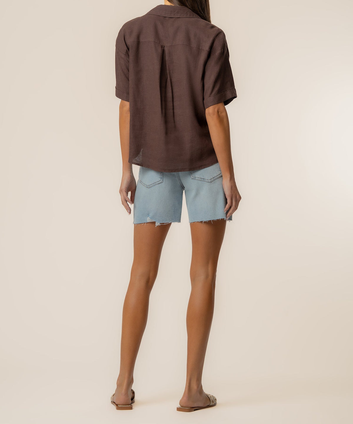 Back view of a woman wearing a brown Brianna Linen Boxy Shirt with light wash denim shorts.