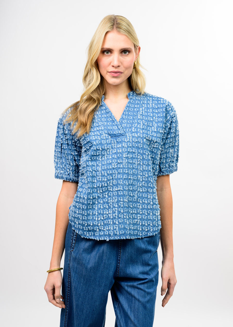 Woman wearing a Jella Distressed Denim Popover with a split V-neck and short puff sleeves.