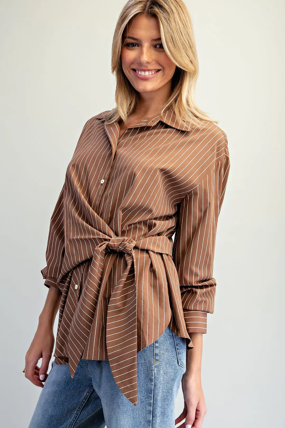 Woman wearing the Reese brown pinstriped blouse with a front tie waist and long sleeves.
