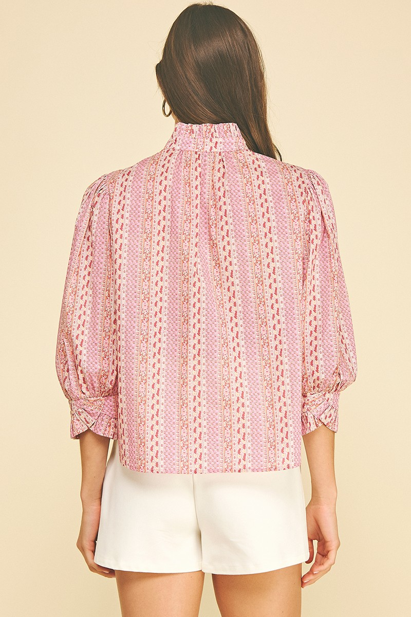 Back view of a woman wearing a pink floral botanical print blouse with a high ruffled collar.