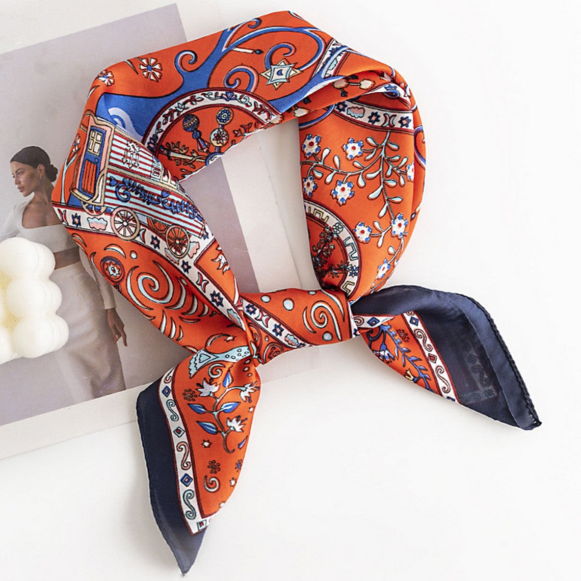 Orange floral satin square scarf with blue and white patterns, knotted on a white surface.