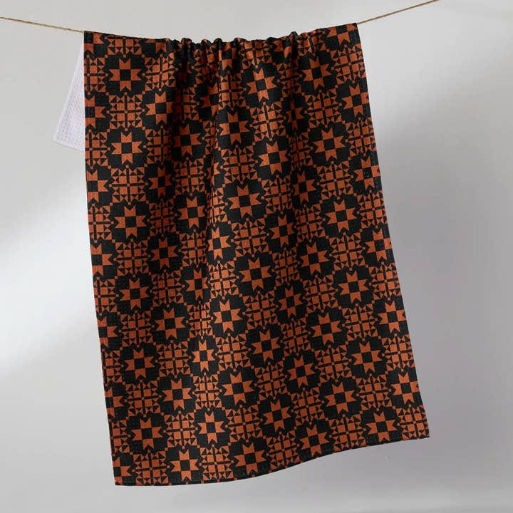 Halloween tea towel with an orange and black geometric star pattern hanging on a line.