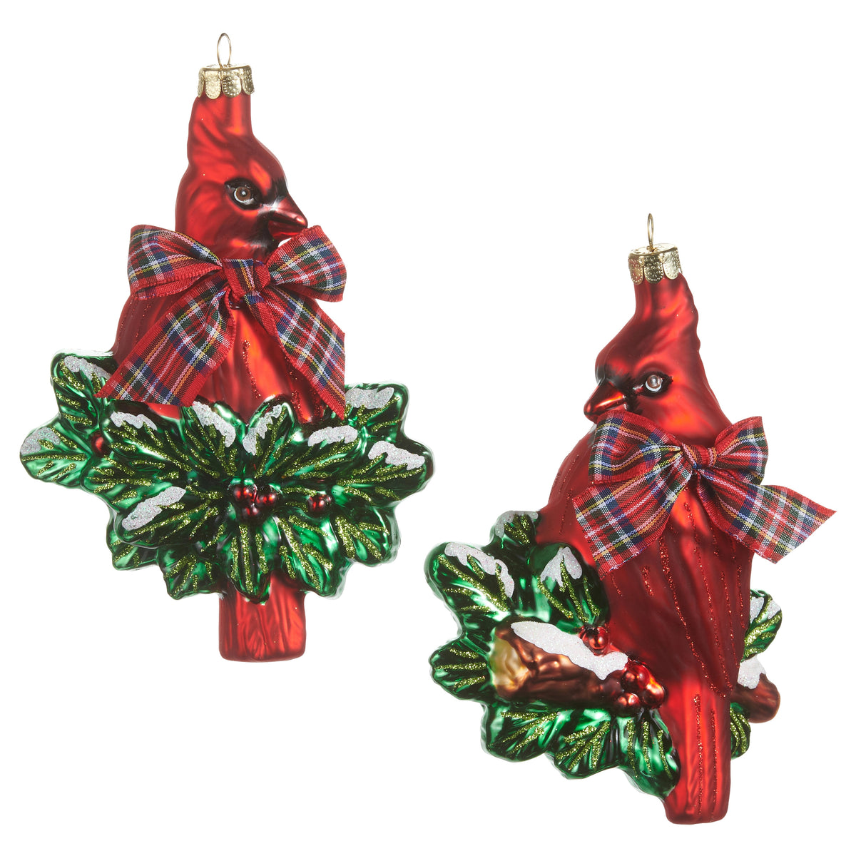Red glass cardinal ornament with a plaid bow perched on snow-dusted holly leaves.
