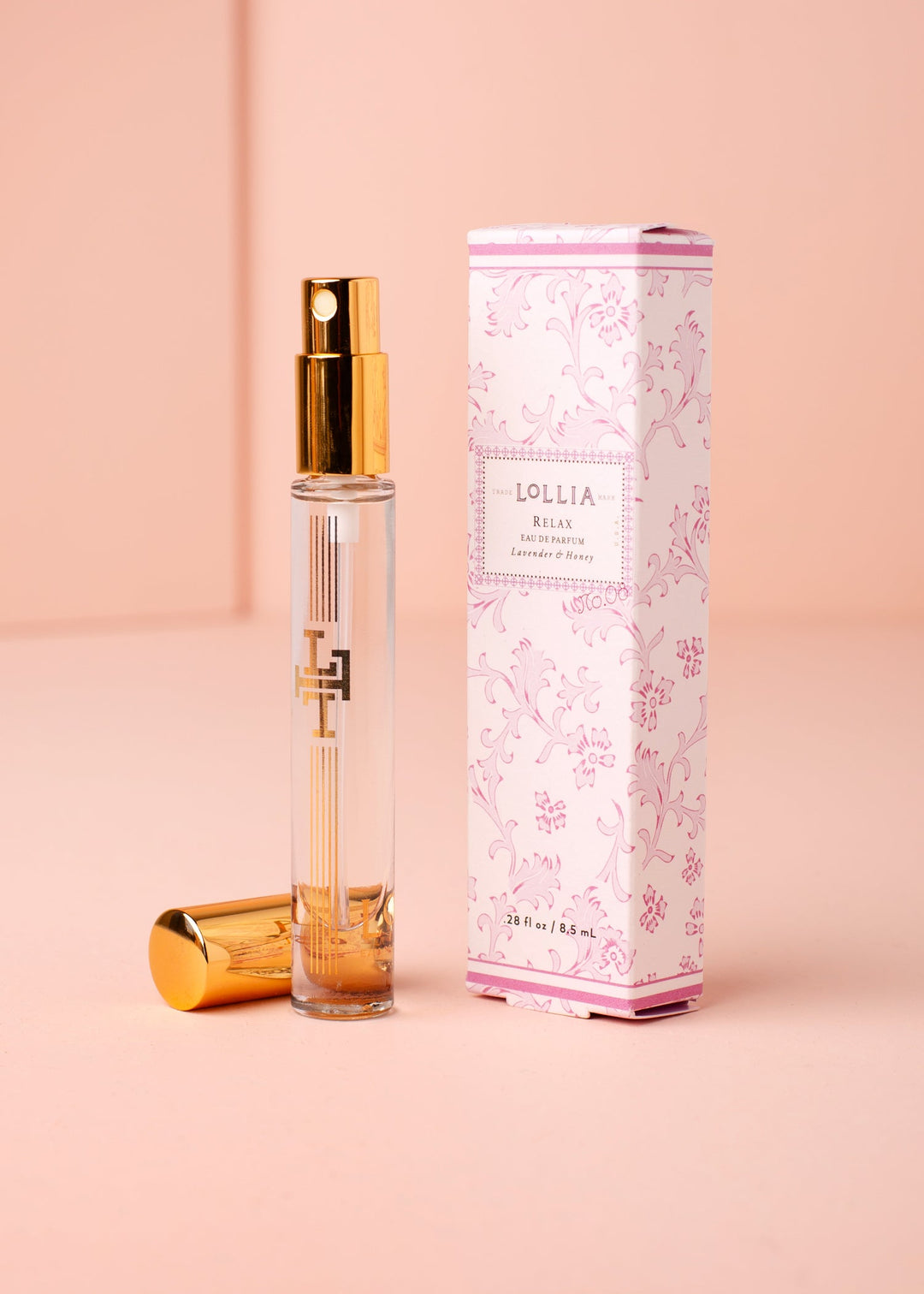 Lollia Relax Travel Eau de Parfum in a gold-accented glass atomizer next to its floral gift box.