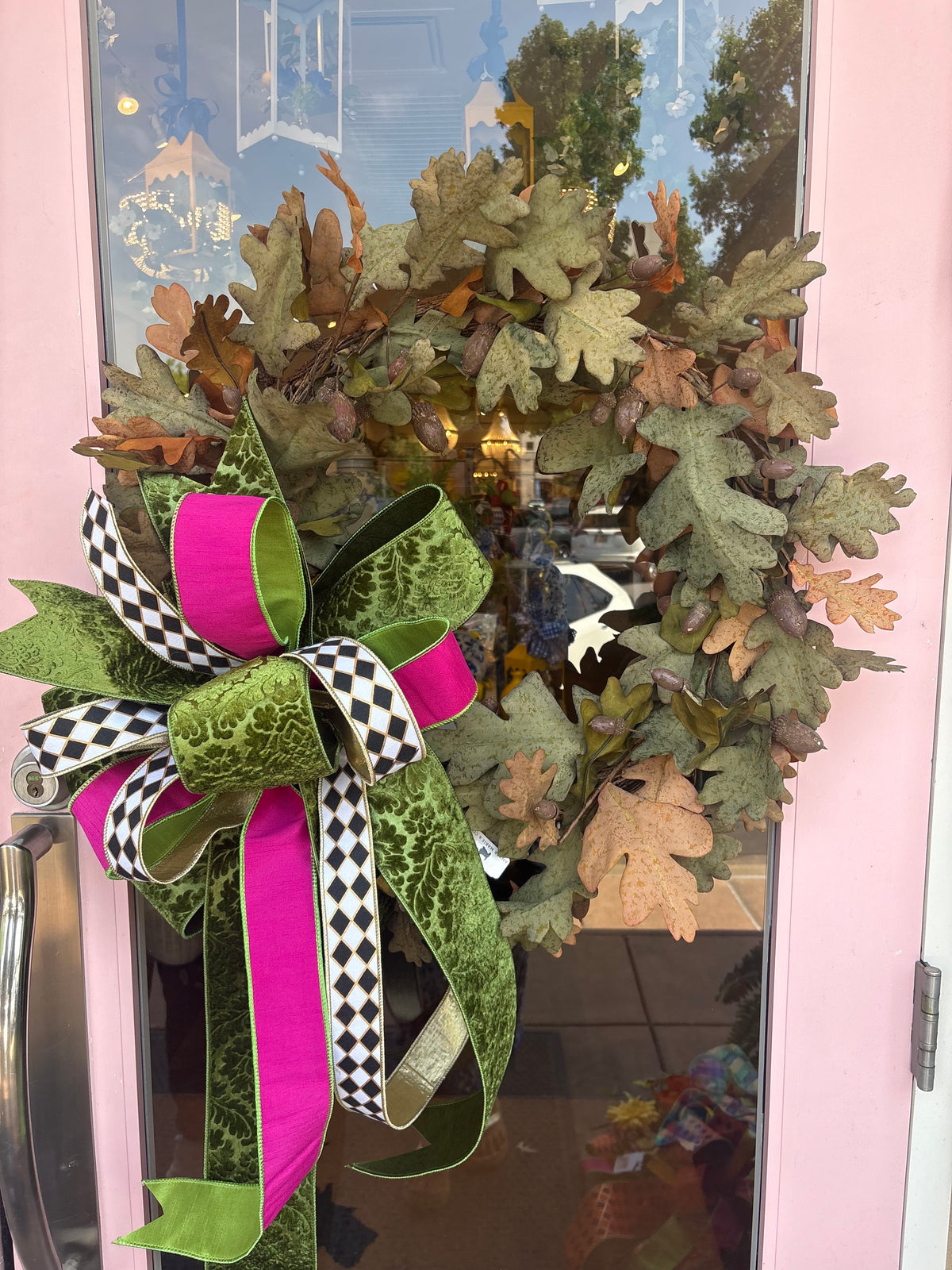 Oak leaf wreath with a large green, pink, and checkered bow on a pink door.