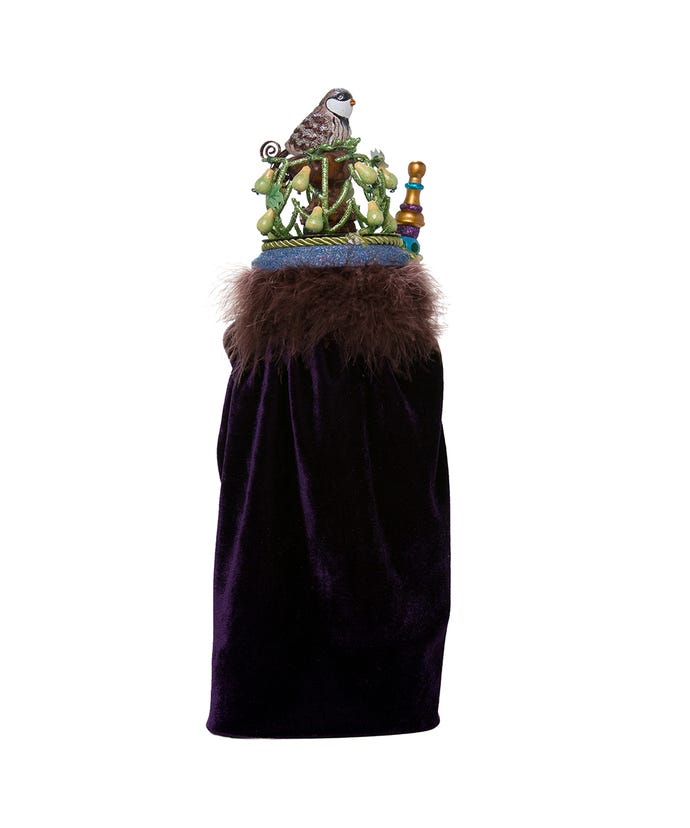 Back view of a nutcracker wearing a purple velvet cape with brown fur trim and a pear tree crown.