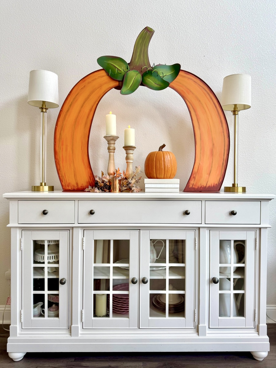 A large orange metal tabletop pumpkin arch decoration displayed on a white sideboard.
