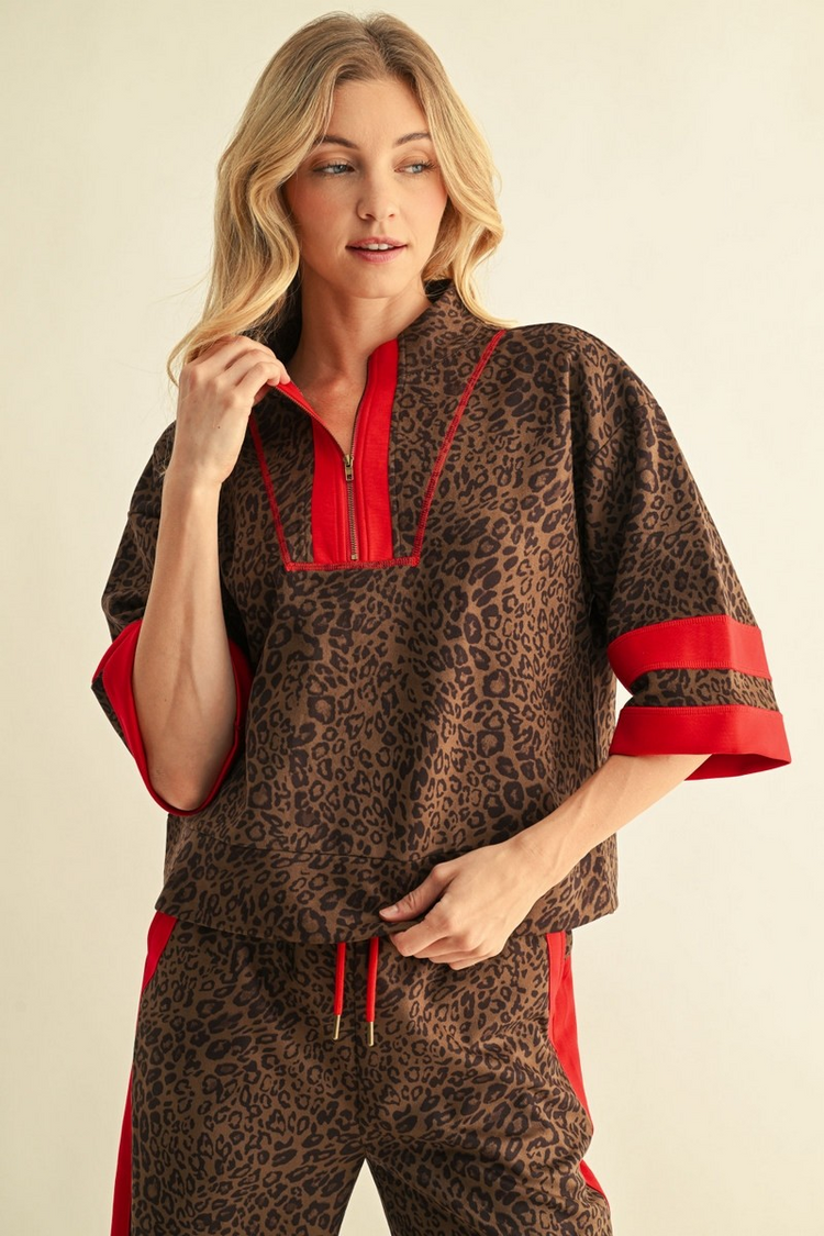 Woman wearing a brown leopard print faux suede top with red trim and a quarter-zip neckline.