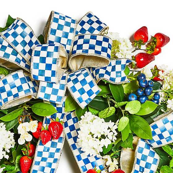 Close-up of a Royal Berry 24" Wreath featuring blue checkered ribbon, red berries, and white flowers.
