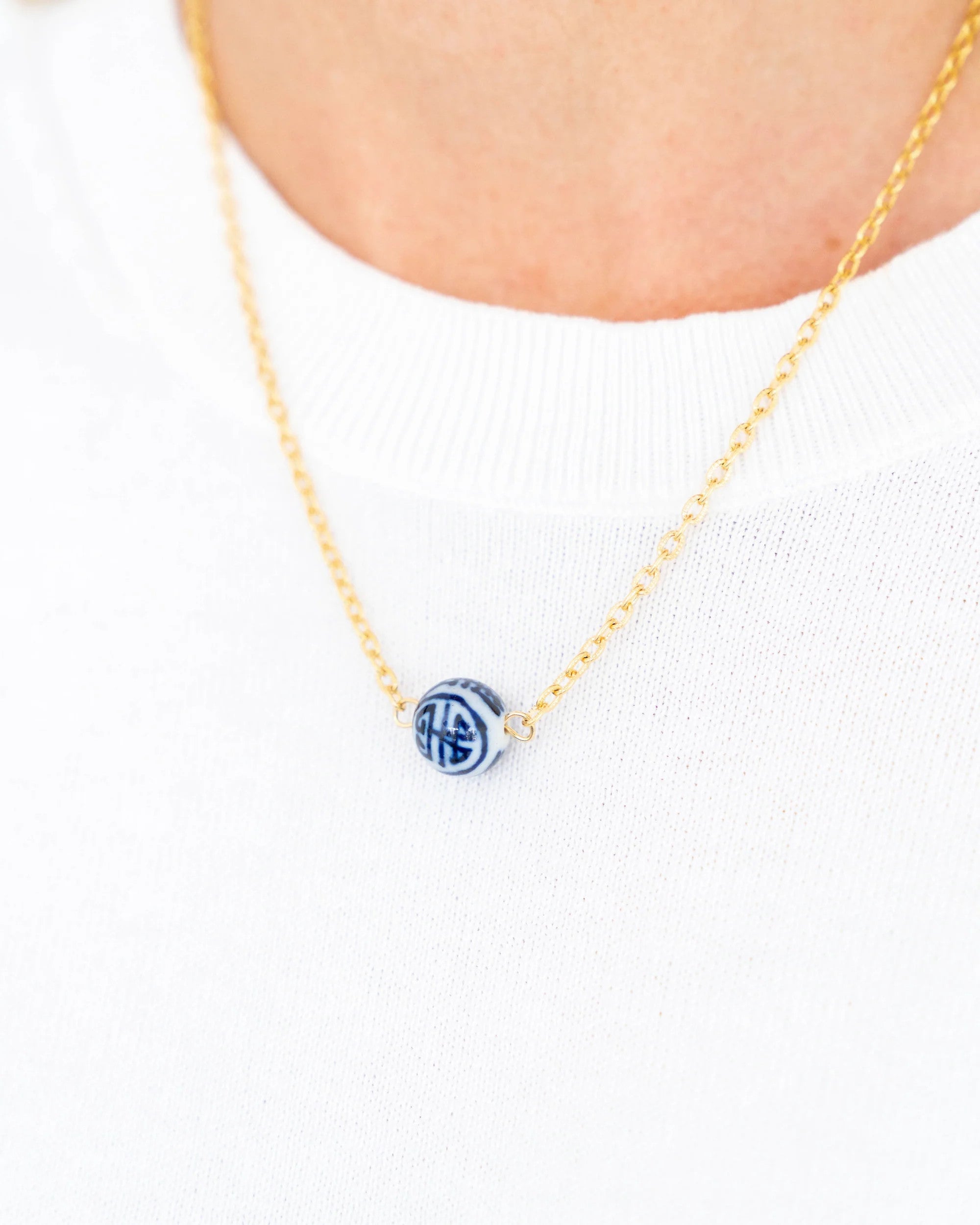 Blue and white hand-painted porcelain bead on a gold-plated chain necklace worn on a person.