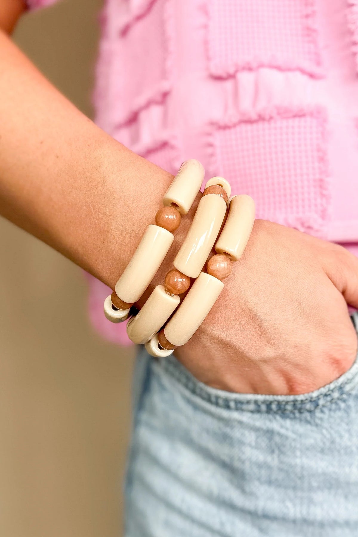 A person wearing three WS Emmy Bracelets with cream acrylic tubes and peach-colored beads.