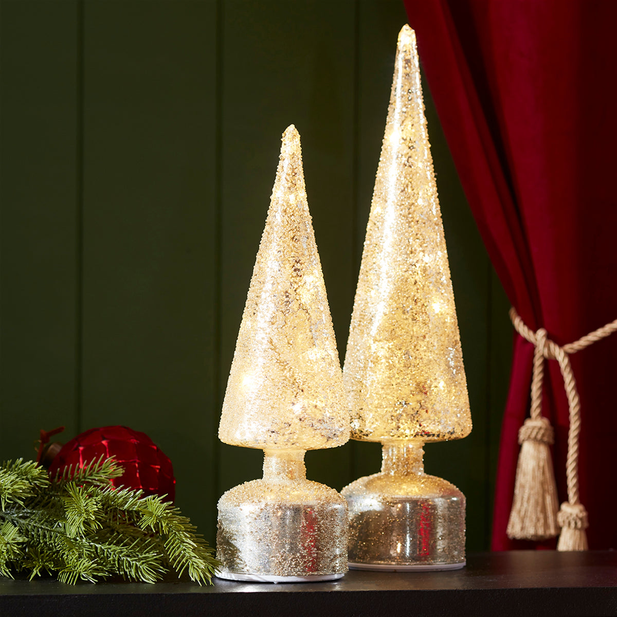 Two glowing, cone-shaped glass LED trees with a rotating base on a dark surface.