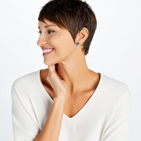 A woman with short brown hair wearing silver-plated Iris Stud Earrings with blue centers.