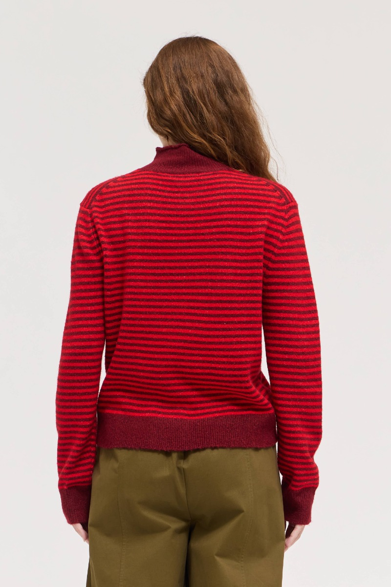 Back view of a woman wearing a red and burgundy striped mock neck sweater with ribbed trim.