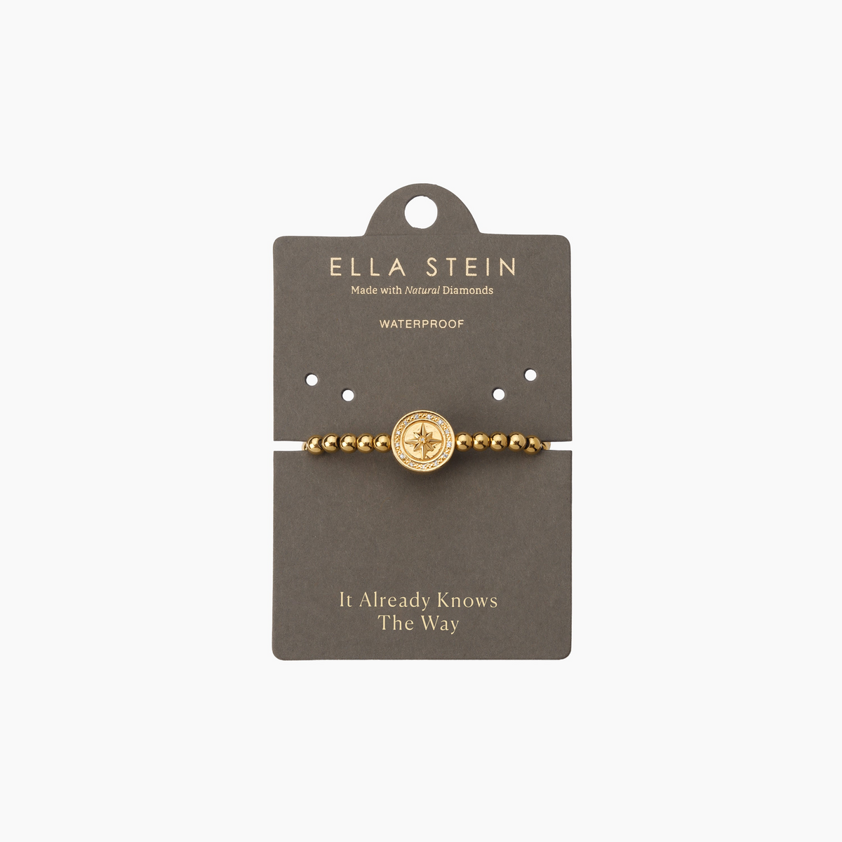 Gold beaded bracelet with a central compass charm on a grey display card.