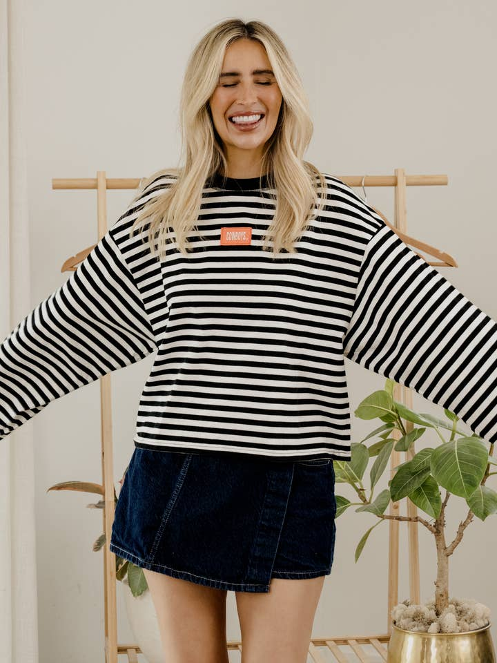 Woman wearing the Althea OSU Cowboys black and white striped long sleeve tee with a denim skort.