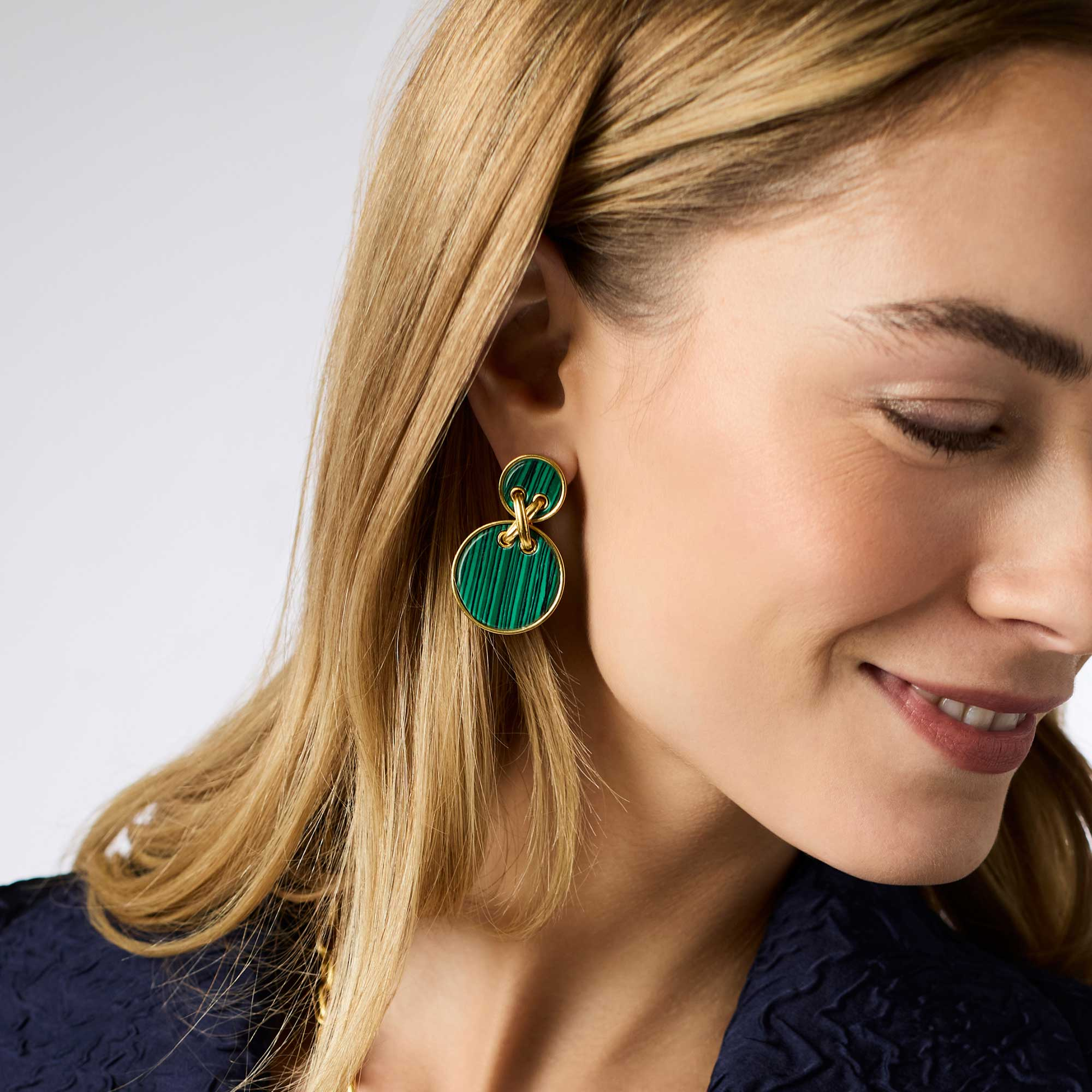 A woman wearing the Essex Statement Earring, featuring two green malachite discs in 24K gold plate.