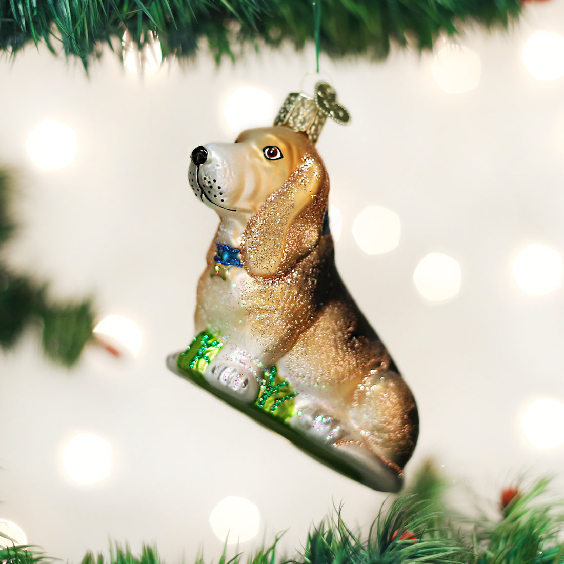 Basset Hound glass Christmas ornament with floppy ears and a blue collar hanging on a tree.