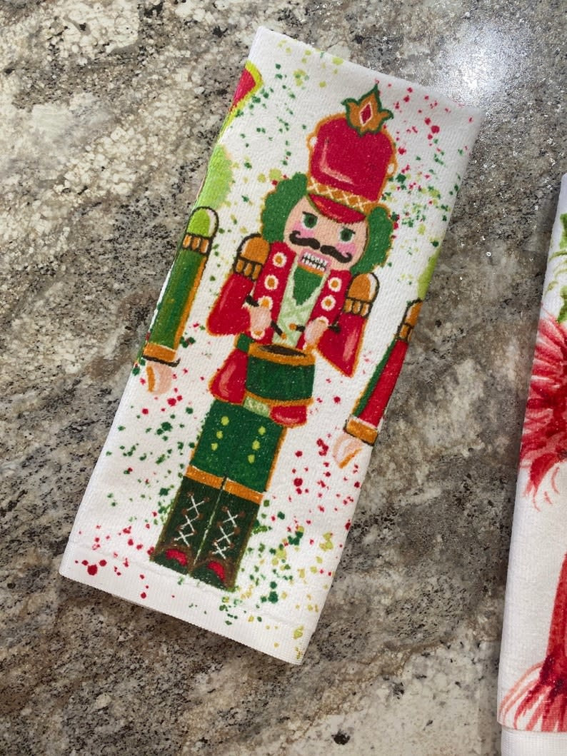 Holiday-themed tea towel with festive red and green patterns on a white background.