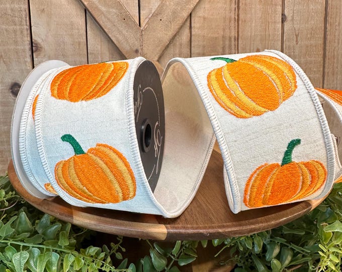 2.5 inch wide beige ribbon with embroidered orange pumpkins on a wooden stand.