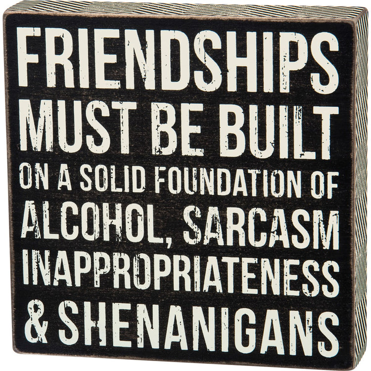 Black wooden box sign with white distressed text reading "Friendships must be built on a solid foundation of alcohol, sarcasm, inappropriateness & shenanigans."