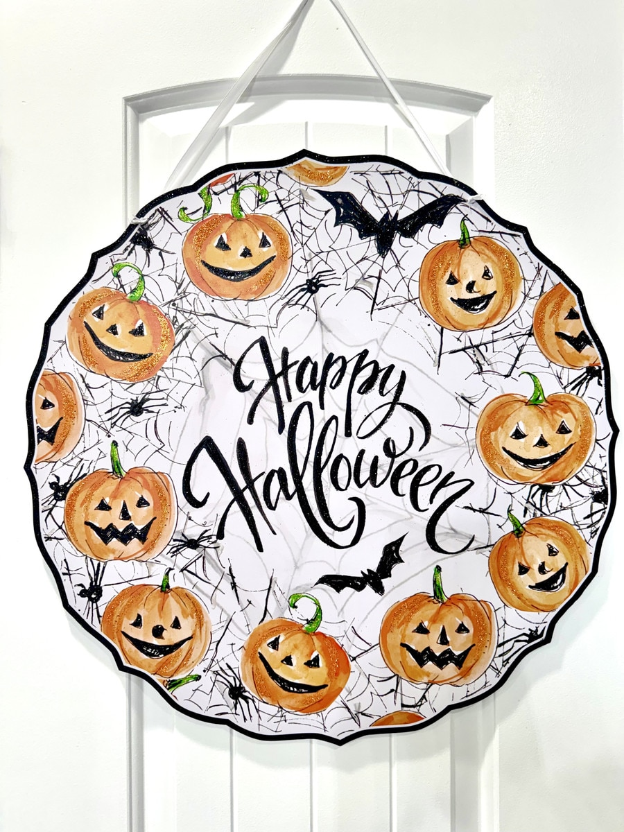 Round PVC door hanger with jack-o'-lanterns, bats, and spiderwebs around "Happy Halloween" script.