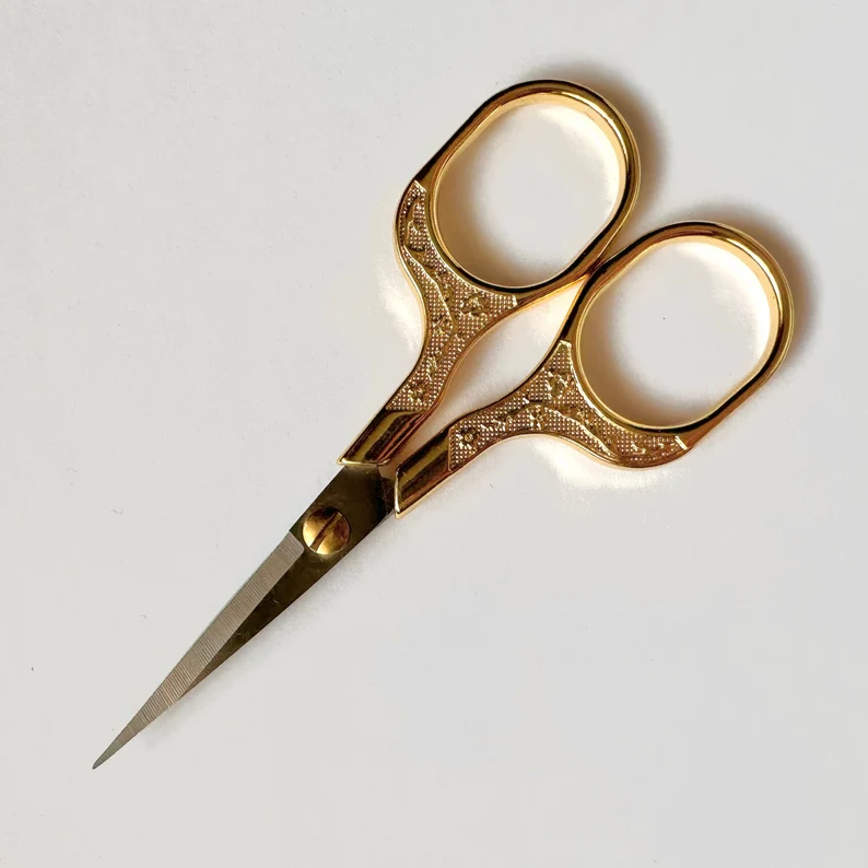 Small embroidery scissors with ornate gold-colored handles and sharp steel blades.