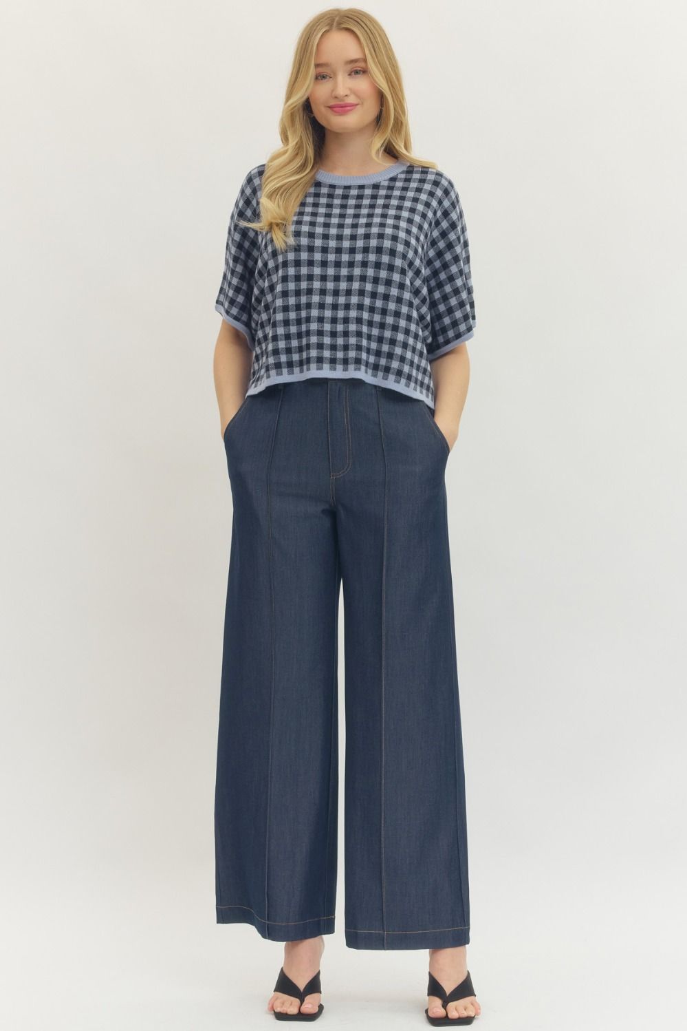 Woman wearing Eleanor Gingham Short Sleeve Cropped Top in blue and black with wide-leg denim pants.