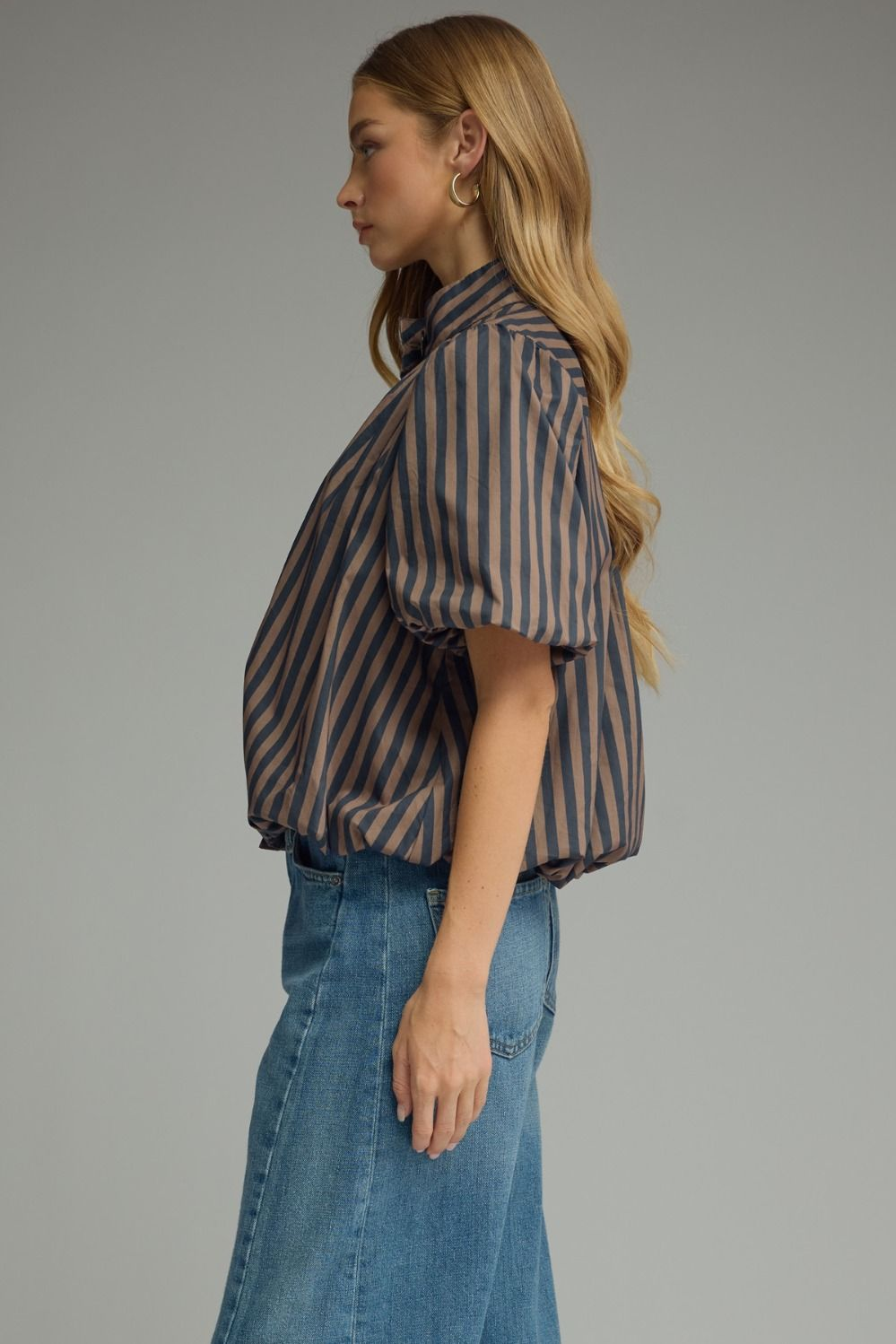 Side view of a woman wearing a brown and navy striped short puff sleeve top with blue jeans.
