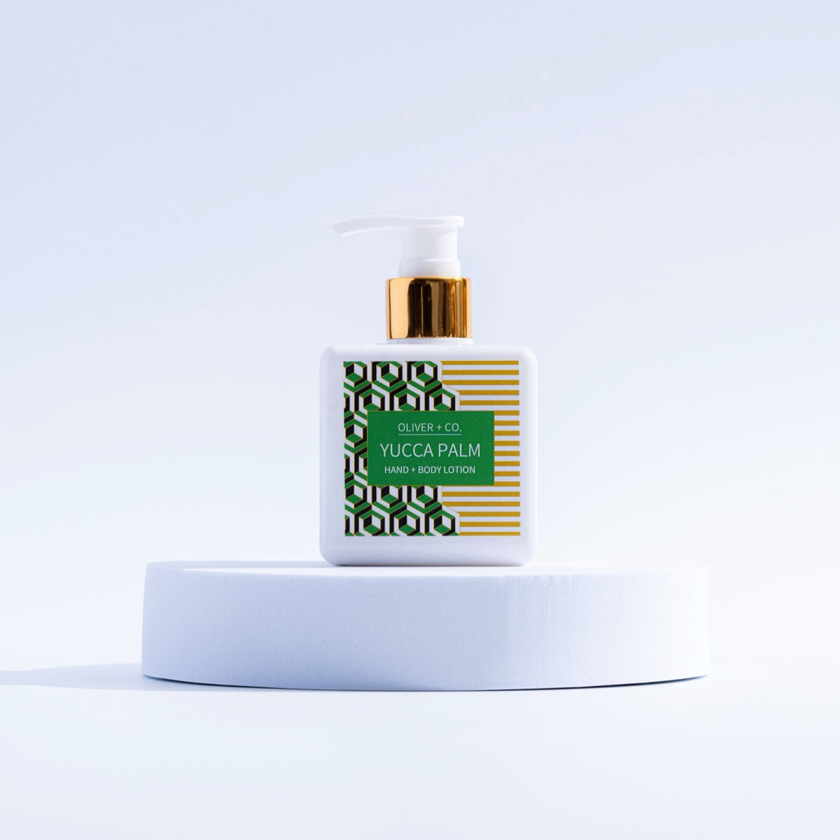 Oliver + Co. Yucca Palm Hand + Body Lotion in a white square pump bottle on a white pedestal.